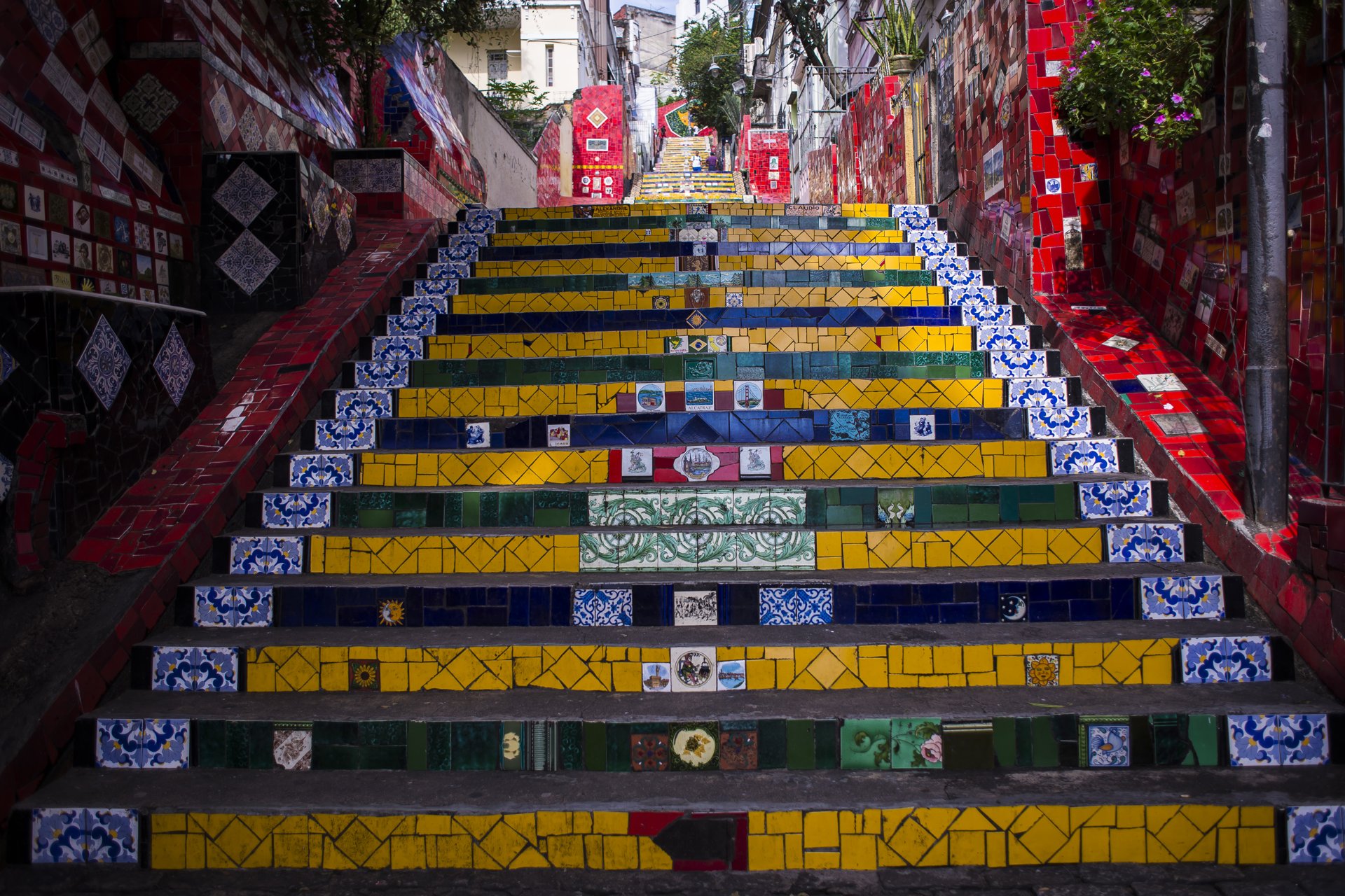 Degraus da Escadaria Selarón cobertos de azulejos amarelos, azuis e verdes, entre paredes vermelhas, na Lapa, Rio de Janeiro
