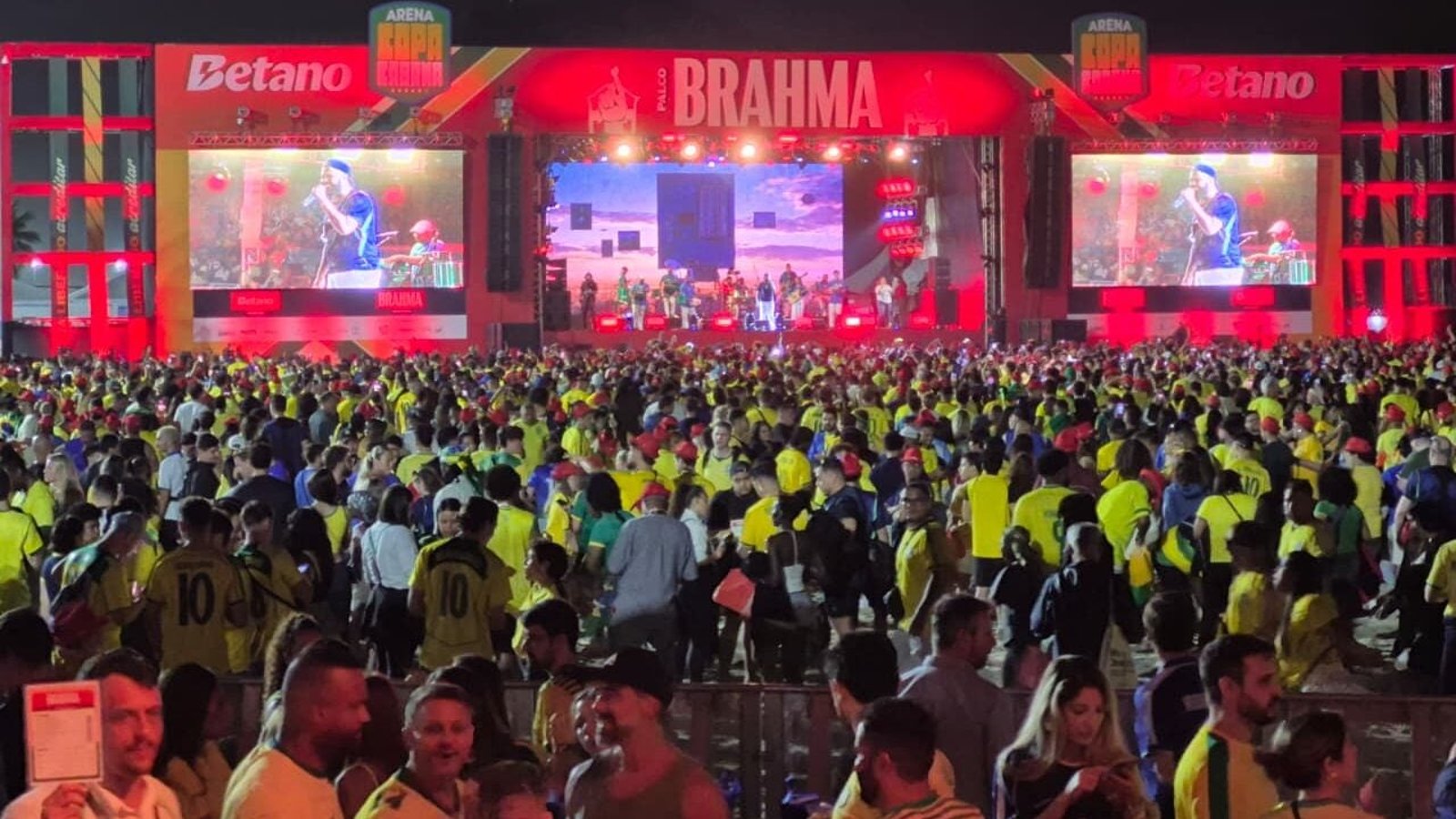 Multidão de torcedores brasileiros lotando a Arena Copacabana da FIFA Fan Festival 2026 durante a estreia do Brasil contra o Marrocos, em 13 de junho, com telões acesos e iluminação noturna